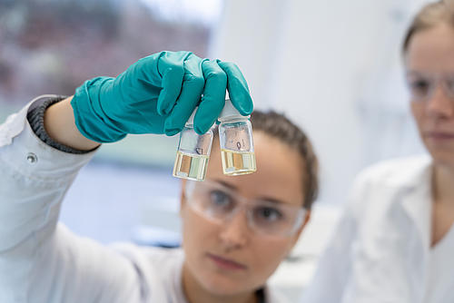 Eine Labor Mitarbeiterin prüft den Inhalt von zwei Fläschchen mit Flüssigkeiten